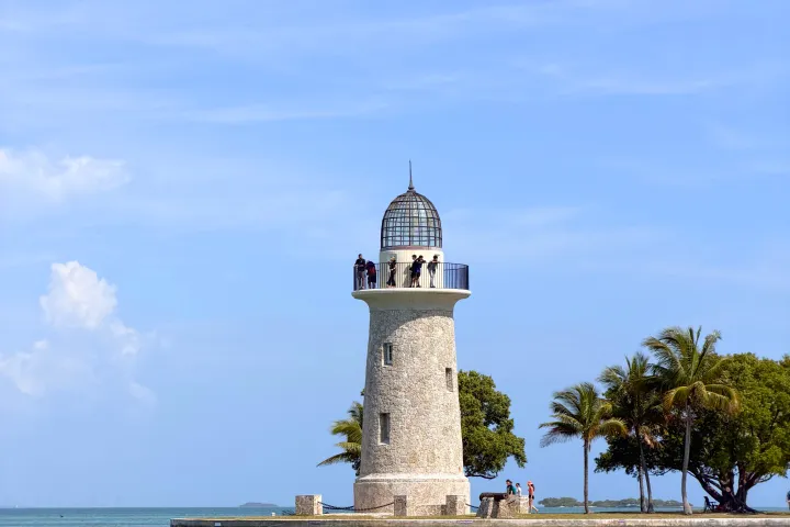 Stone lighthouse on a small island with palm trees and clear blue sky.