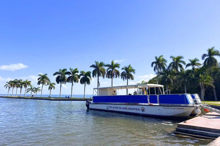 Boat docked at a pier with palm trees and clear blue sky in the background.