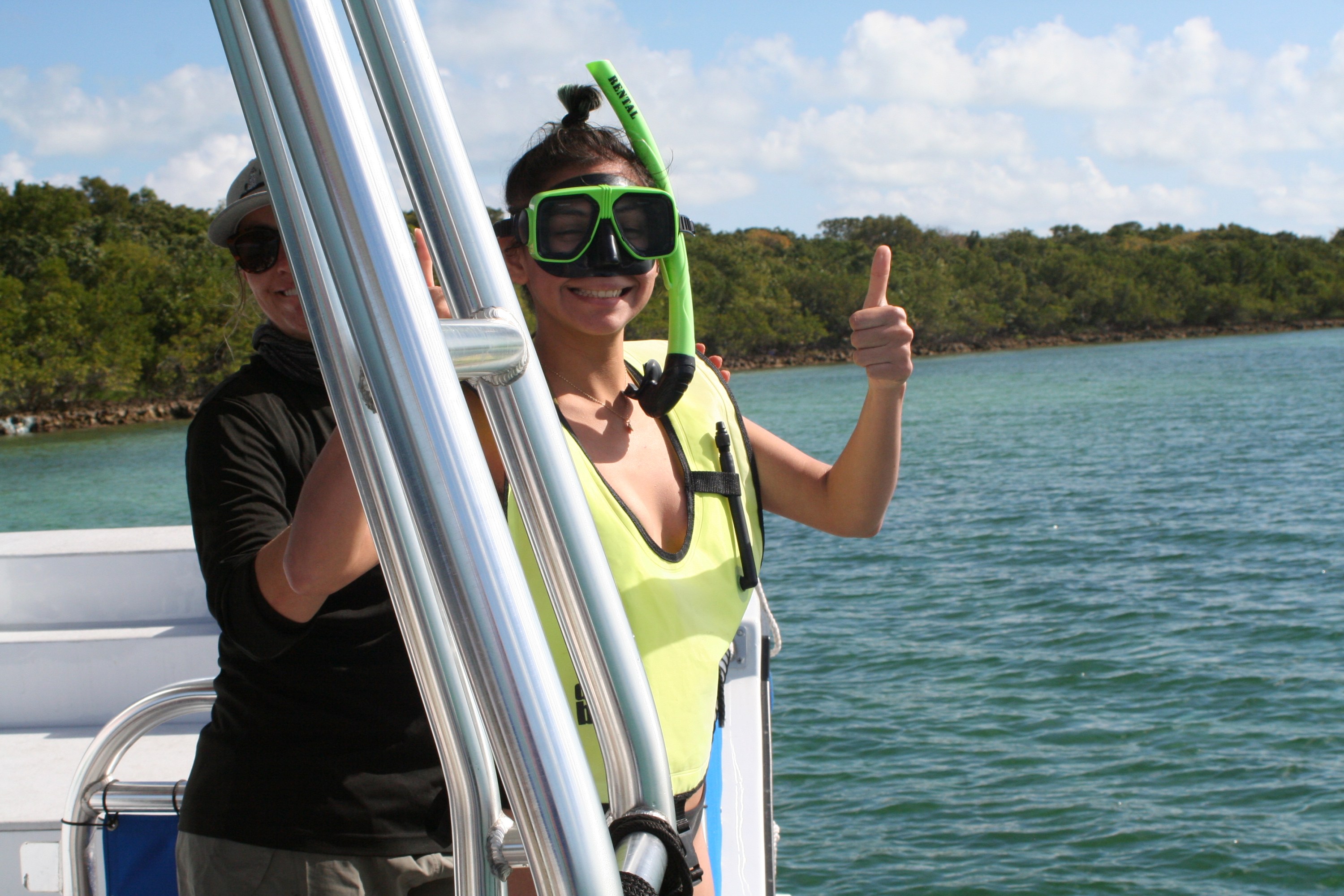 Person on a boat wearing a snorkel and life vest giving a thumbs-up with water and trees in the background.