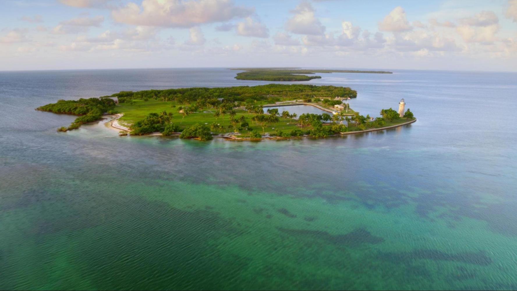 Aerial view of a small tropical island with green vegetation and surrounding blue water.