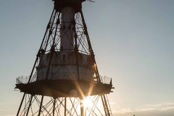 Silhouette of a lighthouse at sunset over the ocean.
