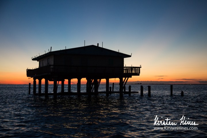 Silhouette of a stilt house over water at sunset.
